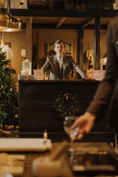 Free Well-dressed man at a retail counter with Christmas decorations, signaling holiday sales. Stock Photo