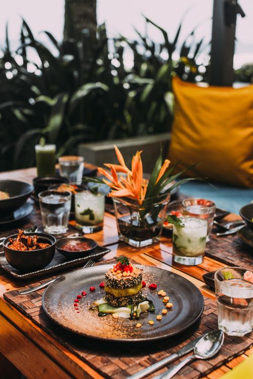 Free Gourmet dish elegantly presented on an outdoor dining table with tropical decor and refreshing drinks. Stock Photo