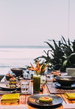A picturesque seaside dining setup with a variety of dishes and beverages on a wooden table.