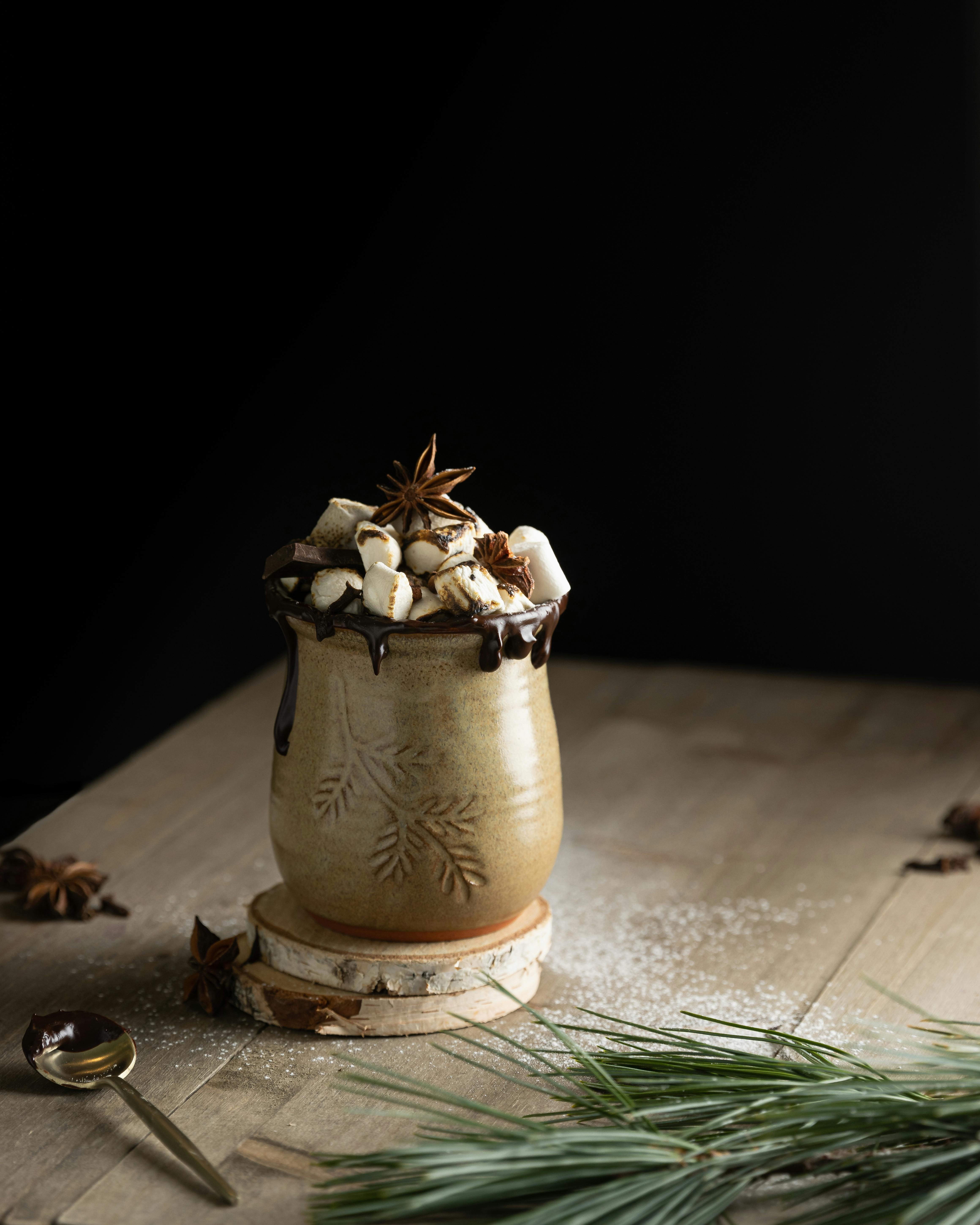 A rustic ceramic mug filled with hot chocolate and marshmallows, garnished with star anise on a wooden table.