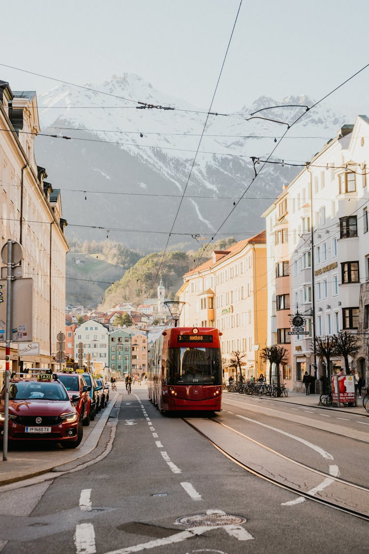 A Tram Passing Parked Vehicles And Buildings