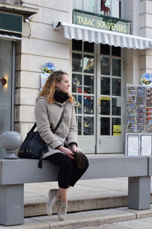 Free Casually dressed woman sitting on a bench outside a souvenir shop in a city. Stock Photo