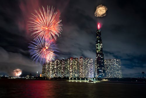 Night cityscape with modern glowing skyscrapers near water with fireworks