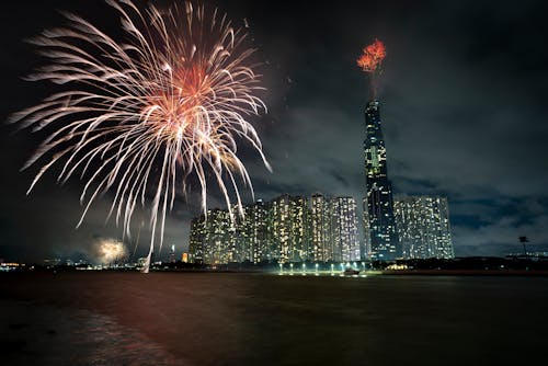 Cityscape with illuminated fireworks and skyscrapers near river at night