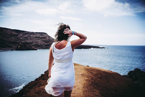 Woman Wearing White Sleeveless Mini Dress on Top of Brown Sand Near Body of Water