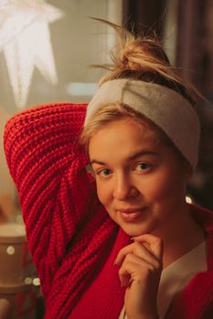 Warm portrait of a smiling woman wearing a red knitted sweater and headband, set in a cozy indoor ambiance.