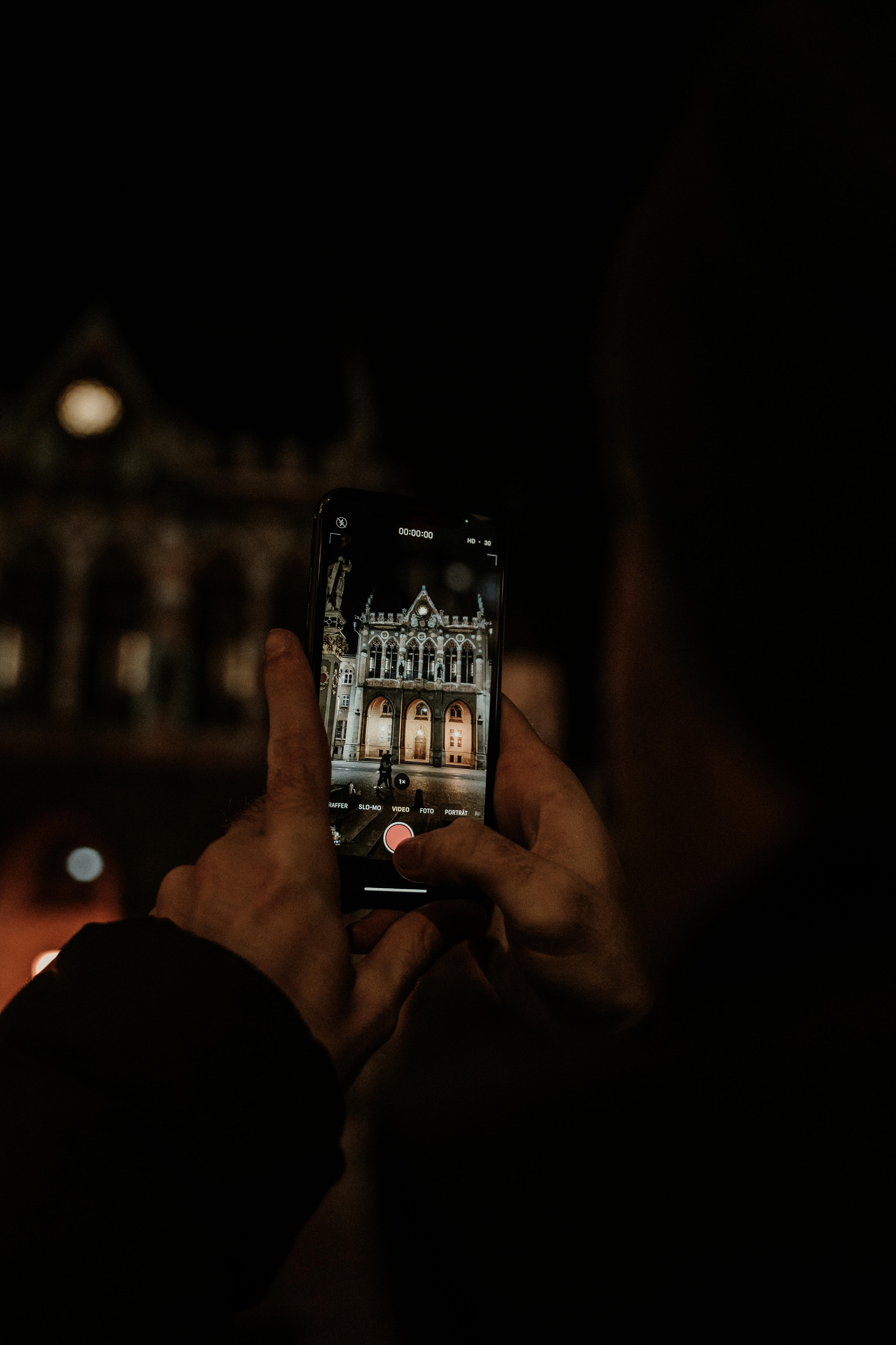 a person holding smartphone taking photo of building during night time