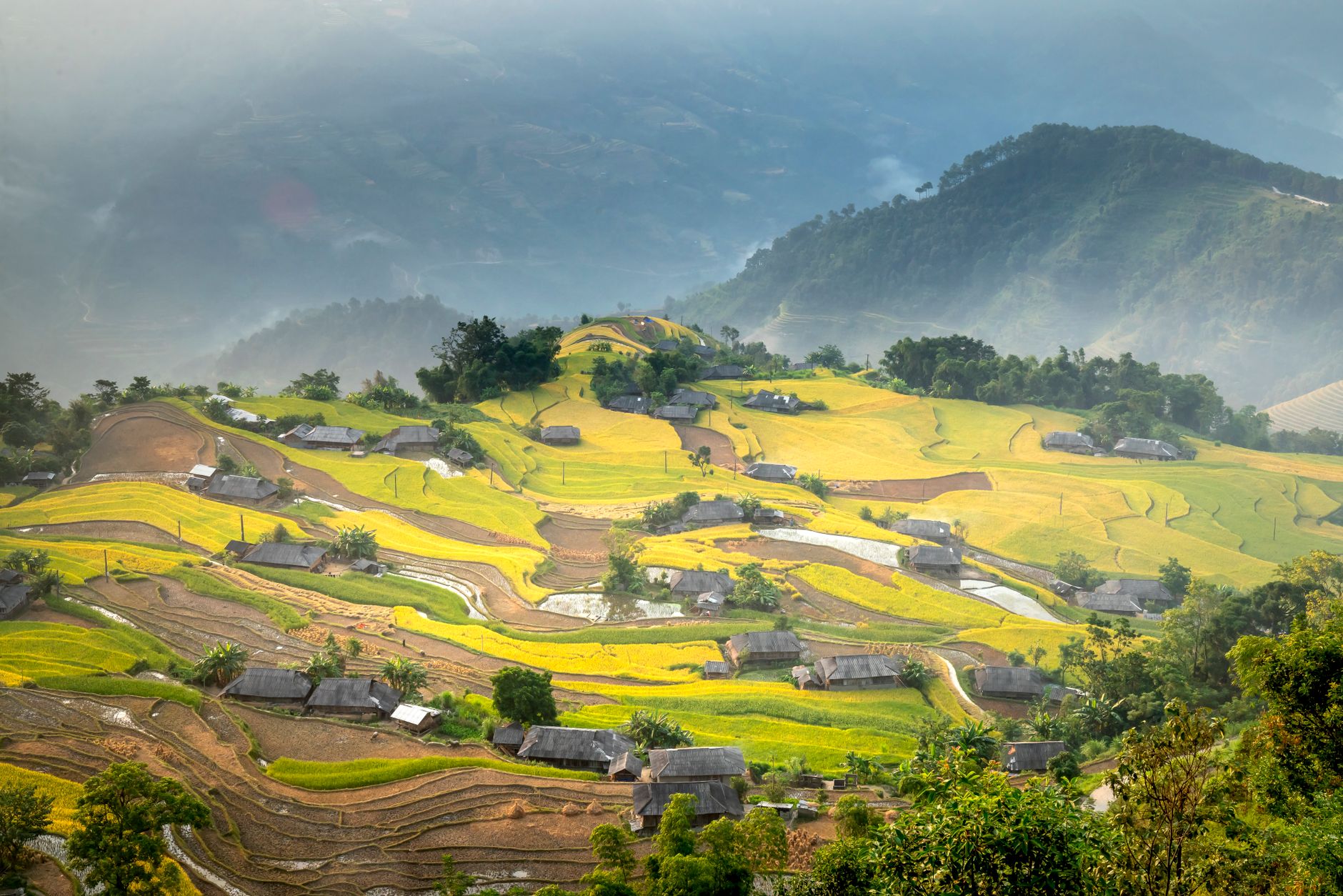 Picturesque view of small remote settlement with green abundant fields located on lush hills on clear summer weather