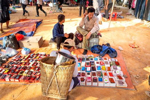 From above of anonymous ethnic male locals sitting on chairs on sandy ground and selling various smartphones on bazaar