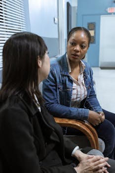 Two women sit in conversation, focusing on serious discussion in an indoor setting.