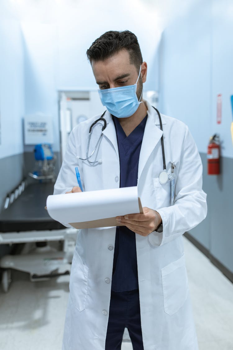 Doctor Writing On A Medical Chart While Standing On The Hallway