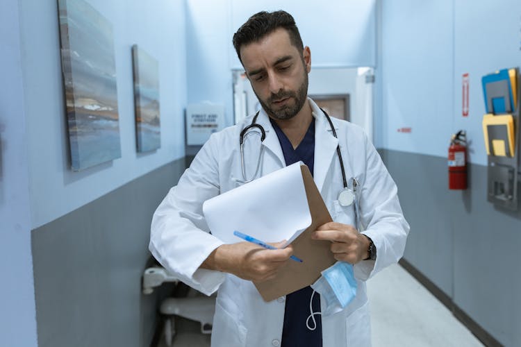 A Doctor In Lab Coat Reading Medical Chart