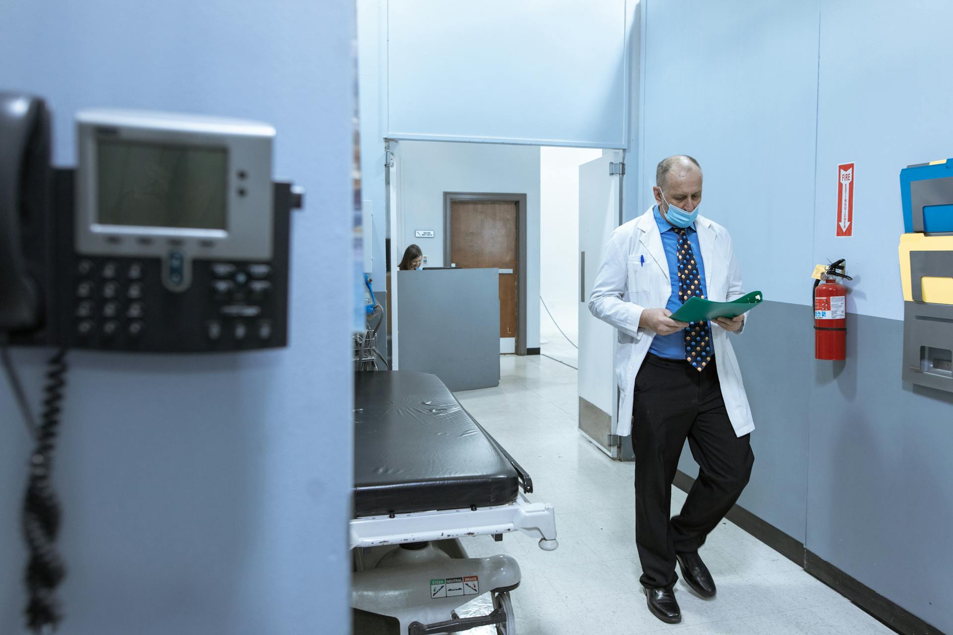 A doctor in a lab coat reads medical files in a hospital hallway, illustrating professional healthcare settings.