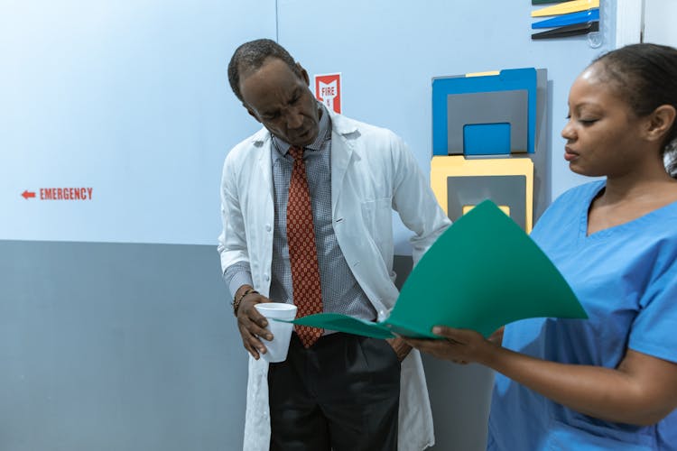 Doctor Reading A Medical Chart Held By A Nurse