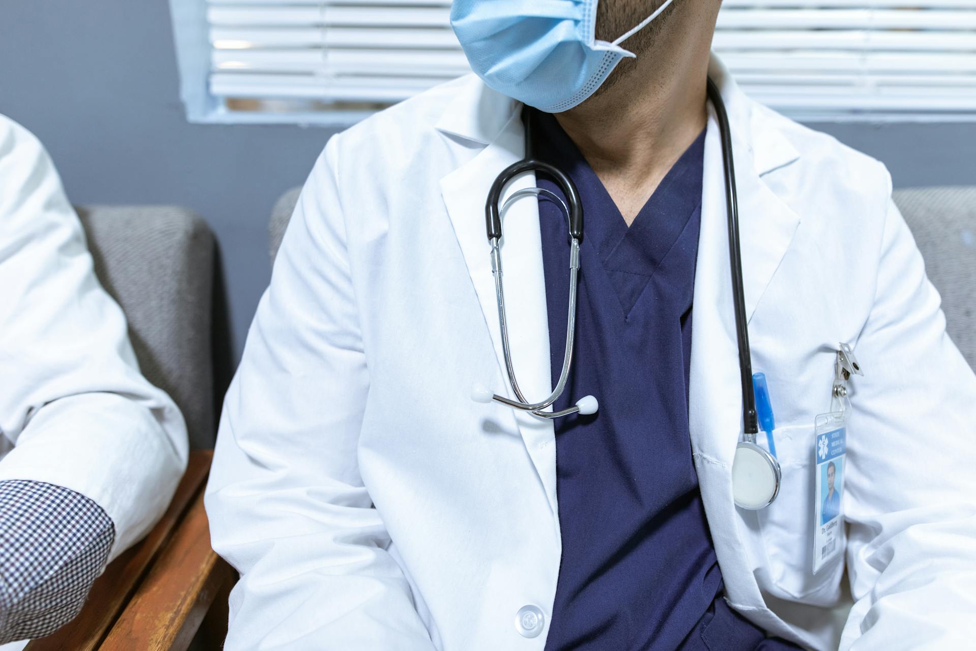 Close-up of a healthcare worker wearing a mask and stethoscope, seated indoors.