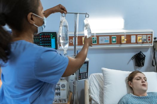 A nurse in a hospital setting adjusts an IV drip for a patient lying in bed, showcasing medical care.