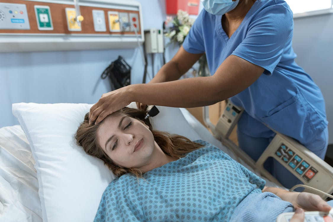Free Crop African American female doctor with professional equipment doing examination of ear of woman lying on bed in hospital ward Stock Photo