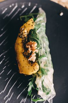 Close-up of a vegan spring roll with pumpkin, walnuts, and greens on a black plate.