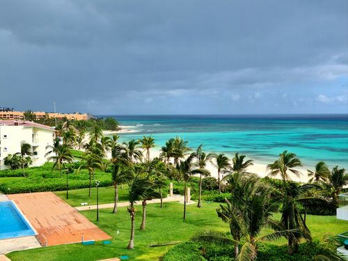 Free Aerial view of a tropical beach resort with lush palms, turquoise ocean, and a swimming pool under a cloudy sky. Stock Photo