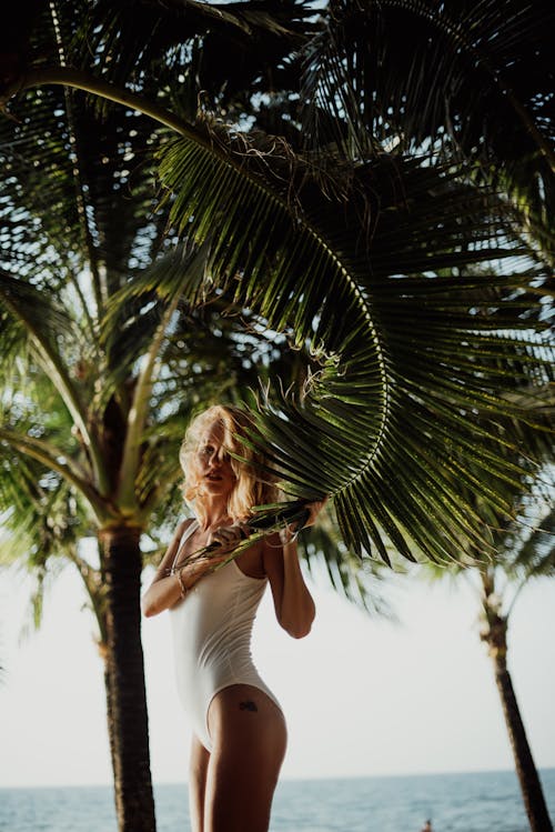 白色背心和白色的褲子，站在綠色的棕櫚樹旁邊的女人