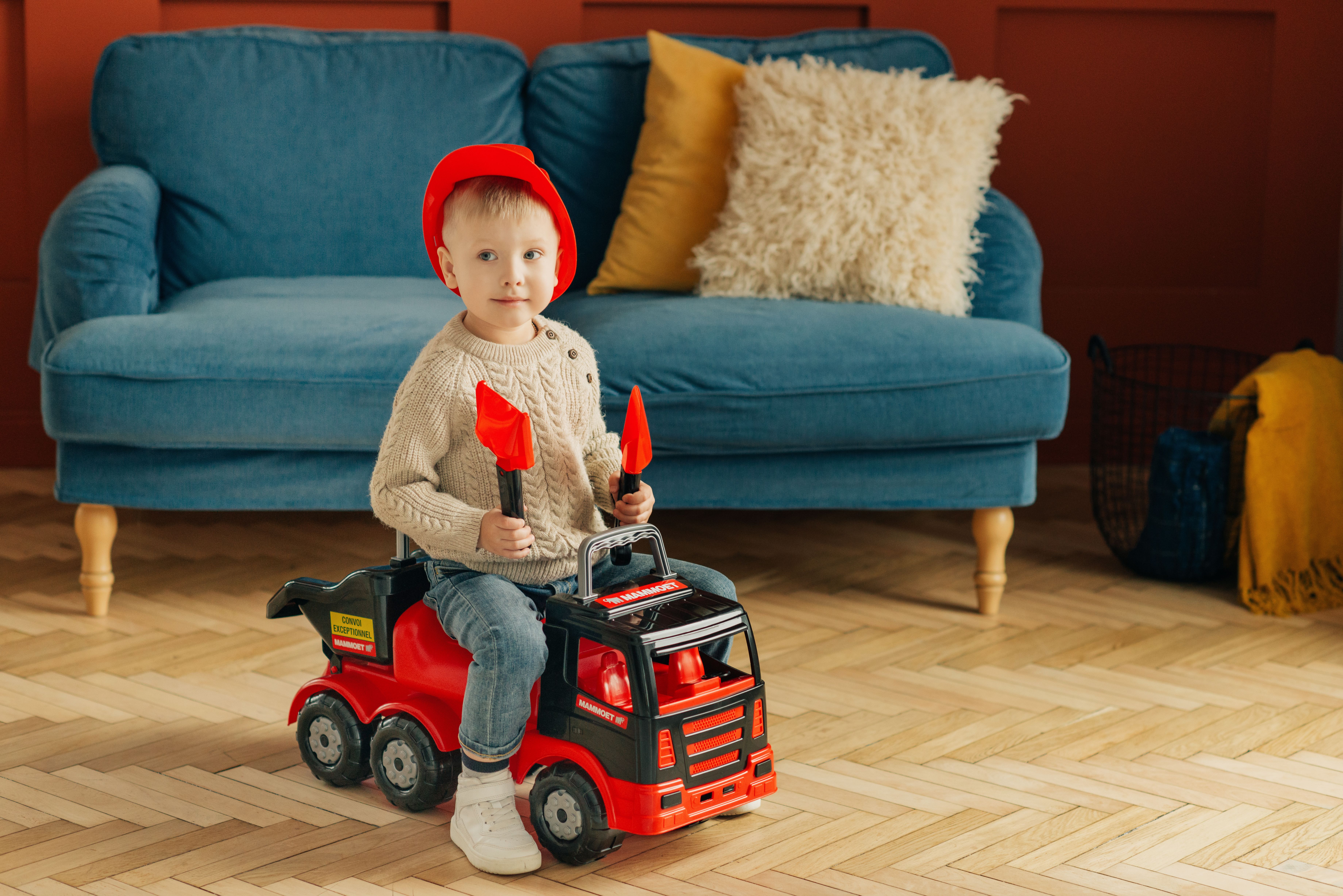 A young boy enjoys playing on a toy truck in a cozy, colorful living room setting. - Photo by Polesie Toys on Pexels