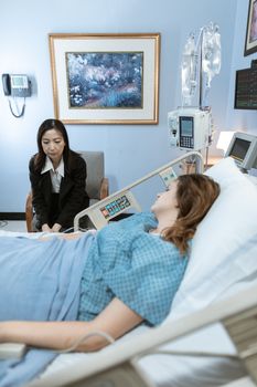 A hospital room showing a patient in bed and a visitor sitting beside her.