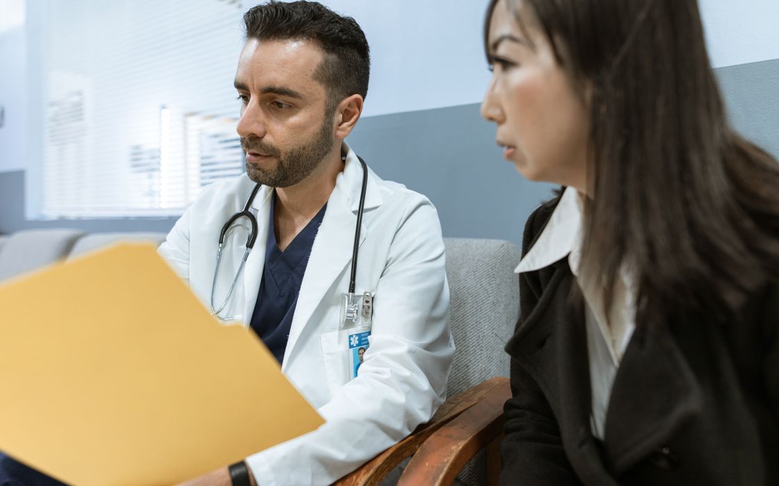 Doctor going through health records in a folder with a female patient during a consultation