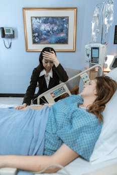 A worried visitor sits beside a patient on a hospital bed, conveying concern and care.