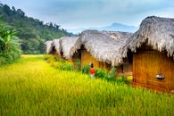 Back view of anonymous kid in small rural village near green grassy hills and trees in daytime under blue sky