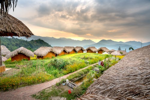 Small houses in settlement near mountains and green grass with pavement in daylight under cloudy sky