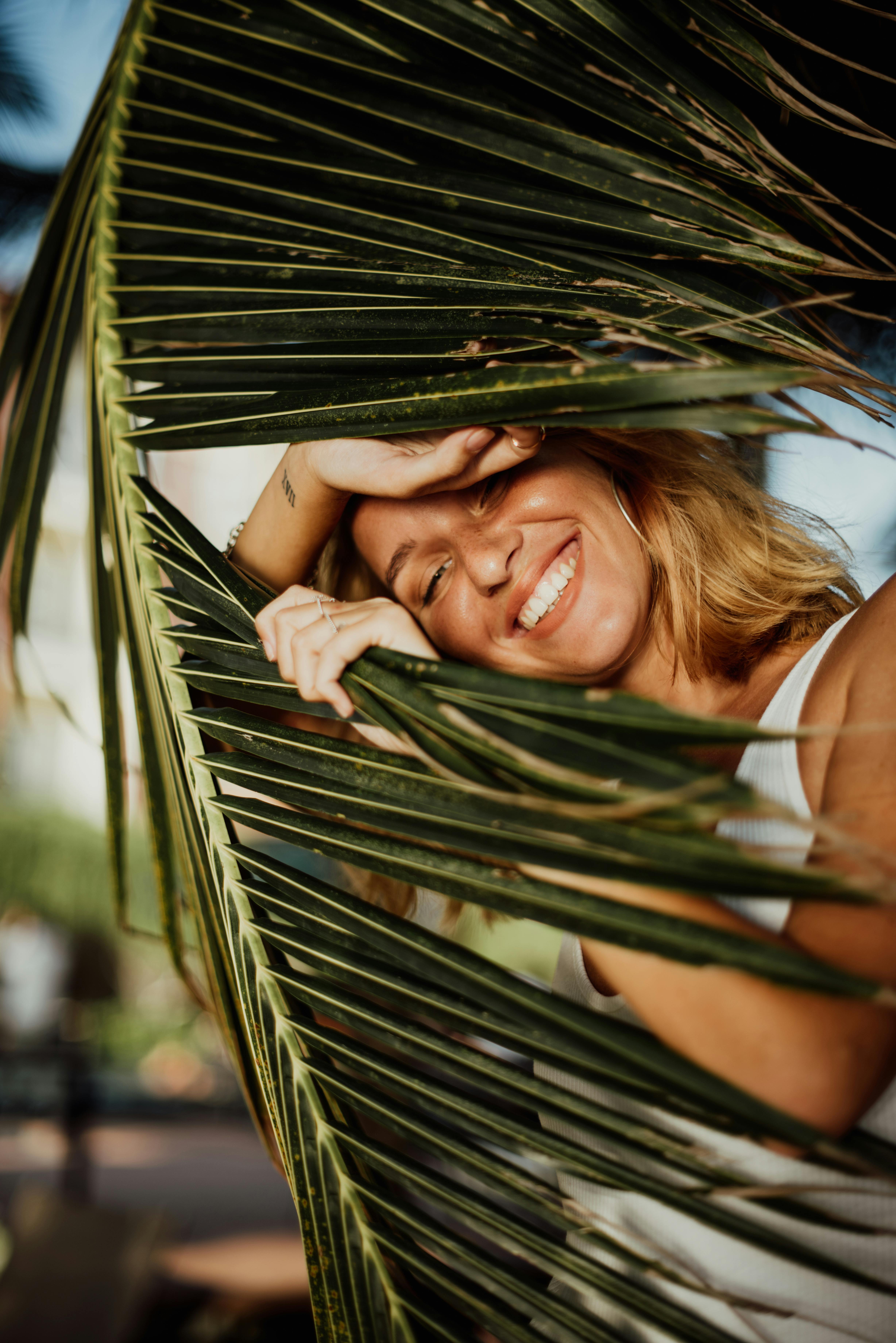 Free Smiling woman with blonde hair enjoying sunny day in Bali with palm leaves in foreground. Stock Photo