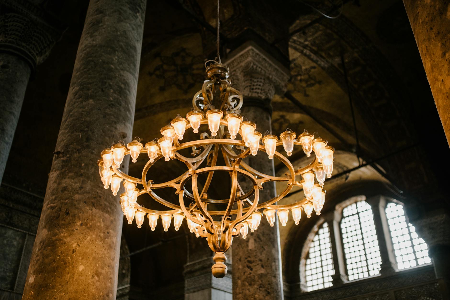 Low angle of old lighting up chandelier hanging from dome with pillars in eastern ancient religious cathedral