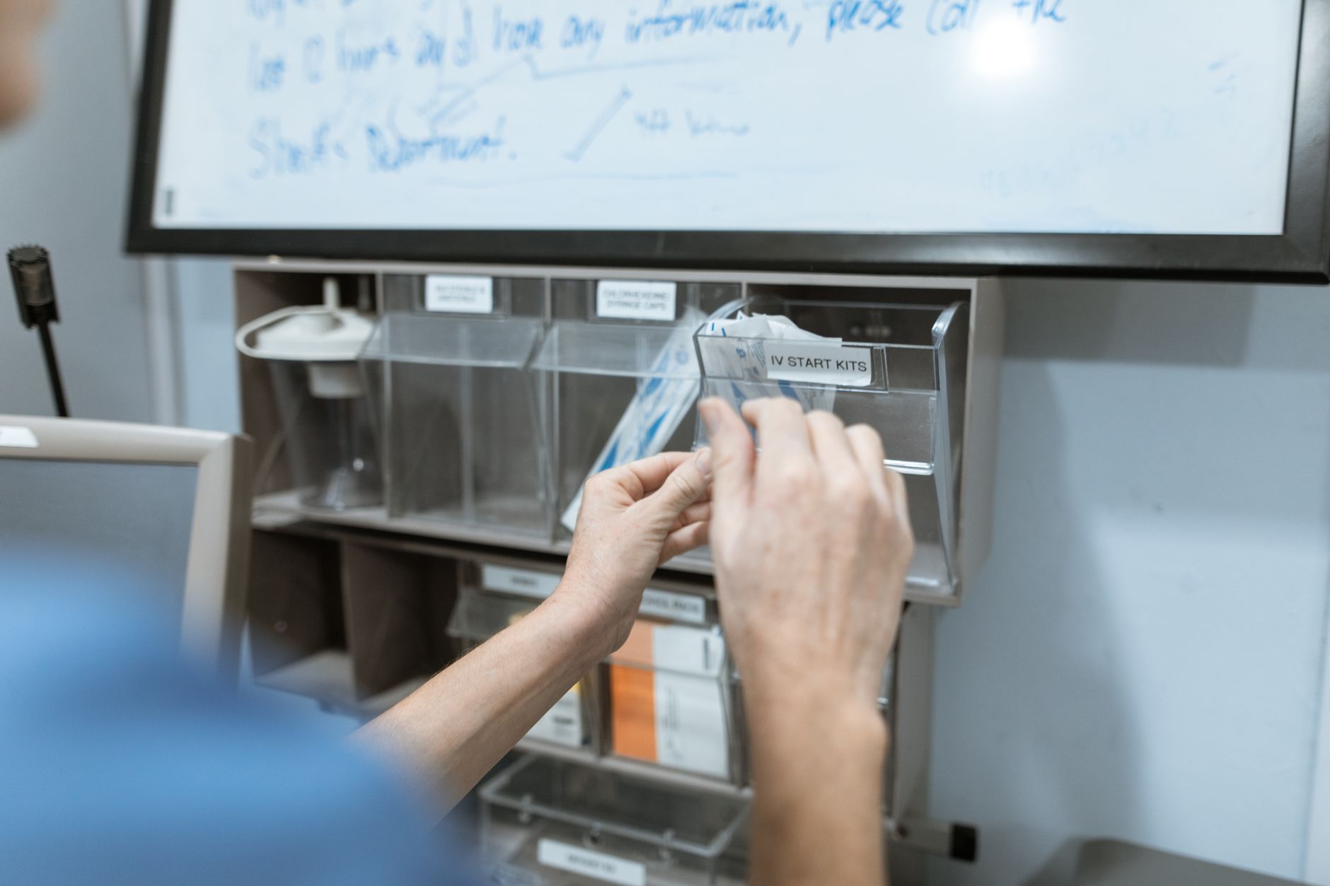 A medical professional selects items from an IV start kit dispenser in a hospital setting.