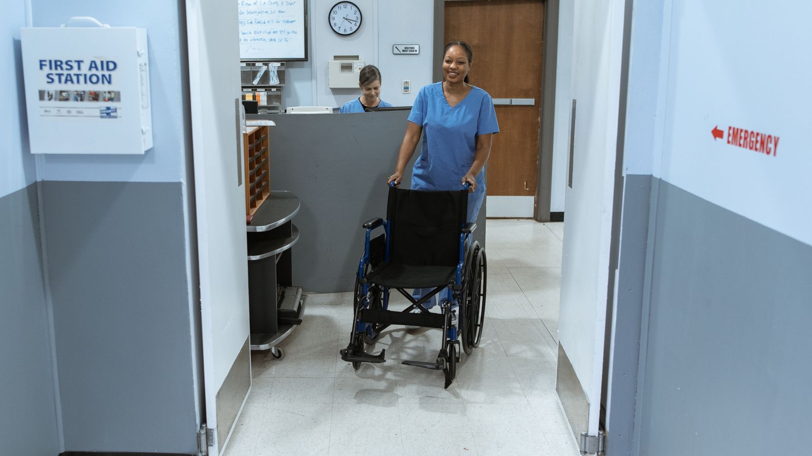 Medical worker pushing an empty wheelchair in a clinical hallway