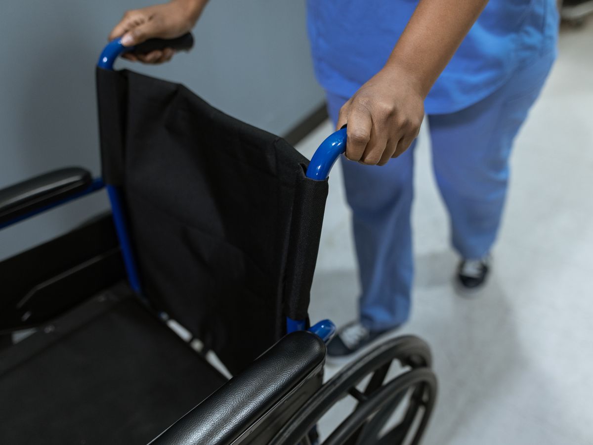Medical worker pushing an empty wheelchair in a clinical setting.