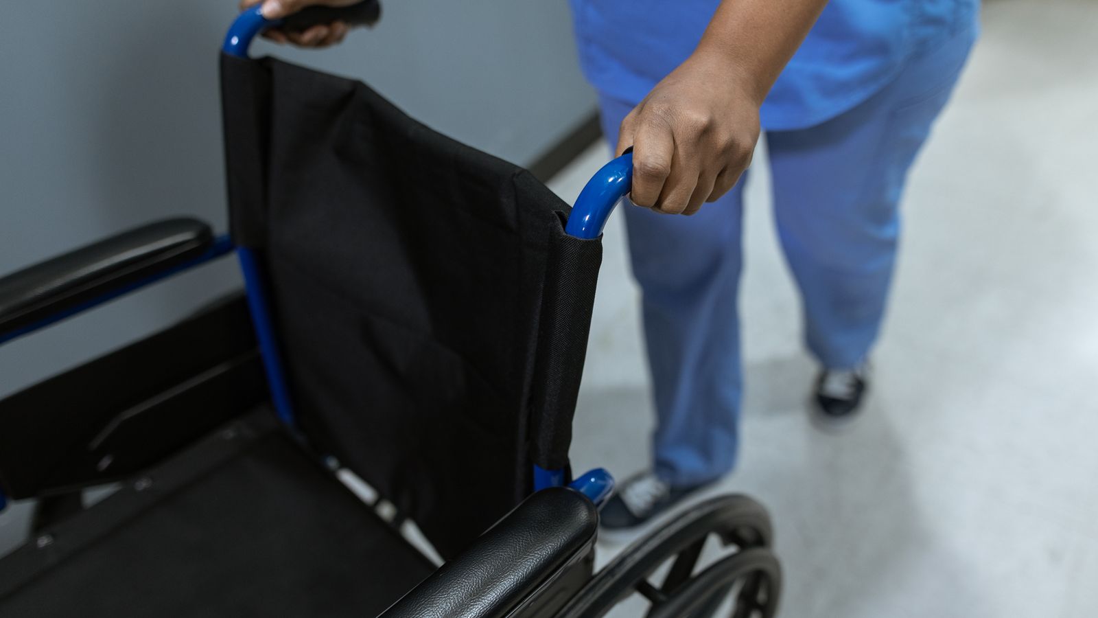 Medical worker pushing an empty wheelchair in a clinical setting.