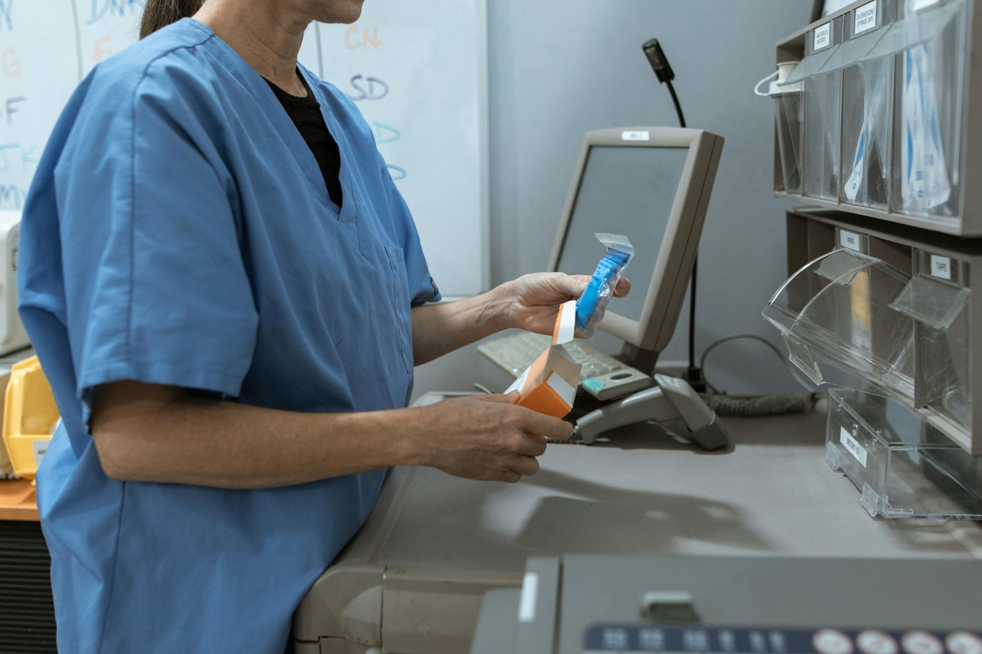 Healthcare worker in scrubs organizing medication in a medical facility.