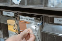 Detail of a hand retrieving alcohol pads from a medical supply dispenser on a shelf.