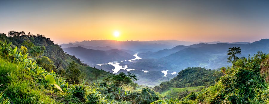 Breathtaking mountain landscape with lush green vegetation and a serene river at sunset.