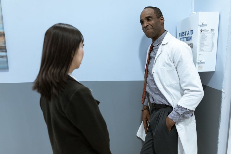 A Black male physician in a white coat talks with a patient in a clinic hallway, the kind of conversation that starts a quit plan with prescription medication and counseling.