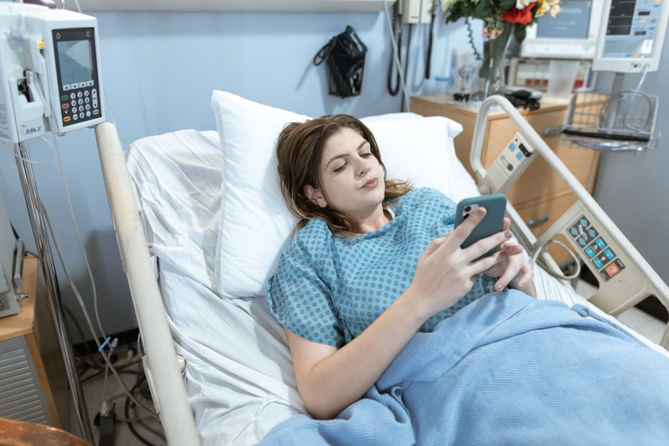 A young woman in a hospital bed using her smartphone while recovering.