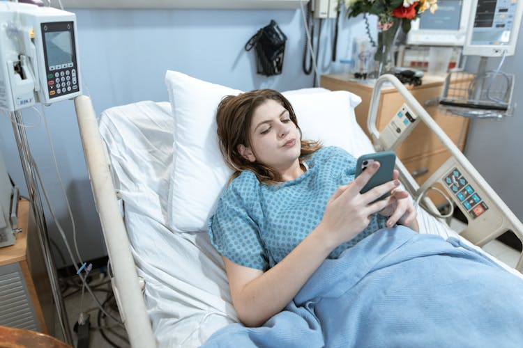 A Woman Using A Smartphone While Lying On A Hospital Bed