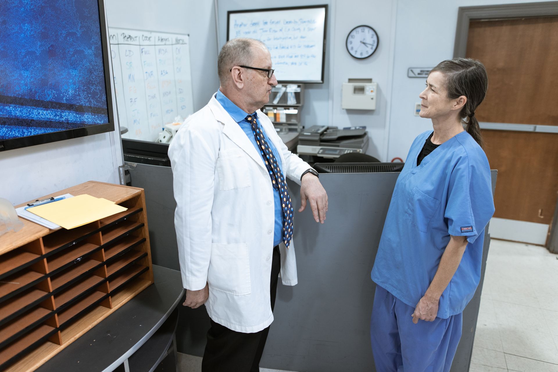 Doctor and nurse in hospital corridor engaging in discussion about patient information and treatment.