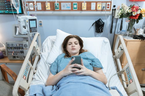 Free Female Patient using Phone while lying on a Hospital Bed  Stock Photo