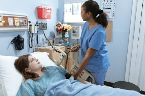 Femme En Costume De Gommage Bleu Tenant Un Lit D'hôpital Blanc Et Gris