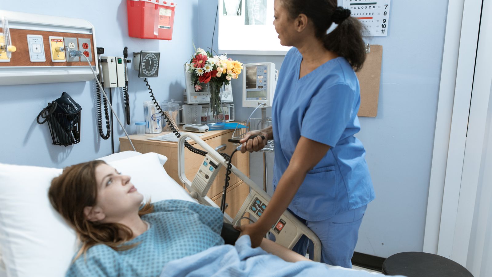 Nurse providing care to a patient in a hospital room with medical equipment.