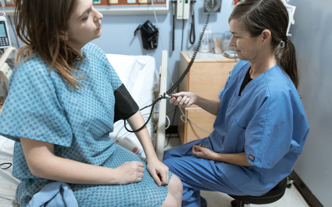 A nurse checks a female patient's blood pressure in a hospital room before a procedure