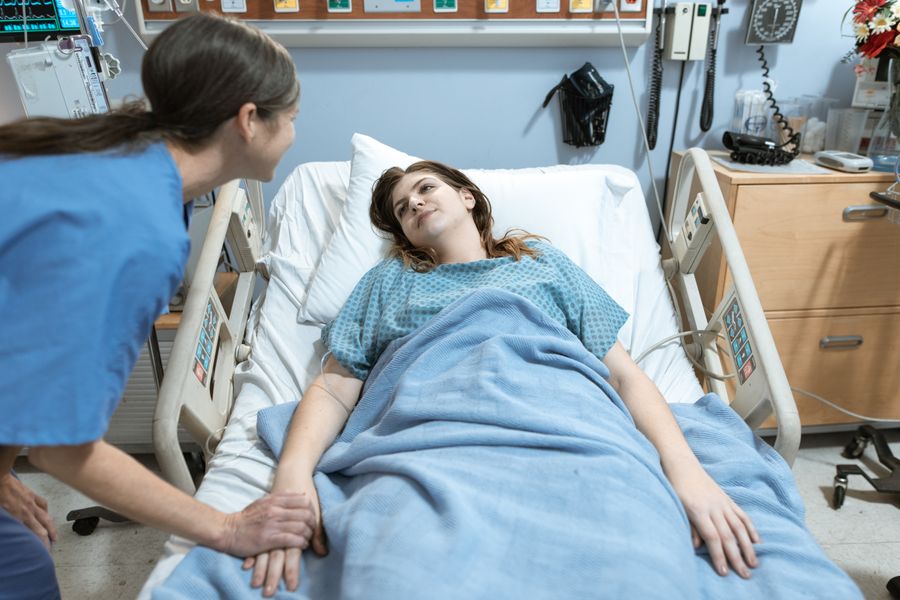 A caregiver gently holds a patient's hand while they talk.