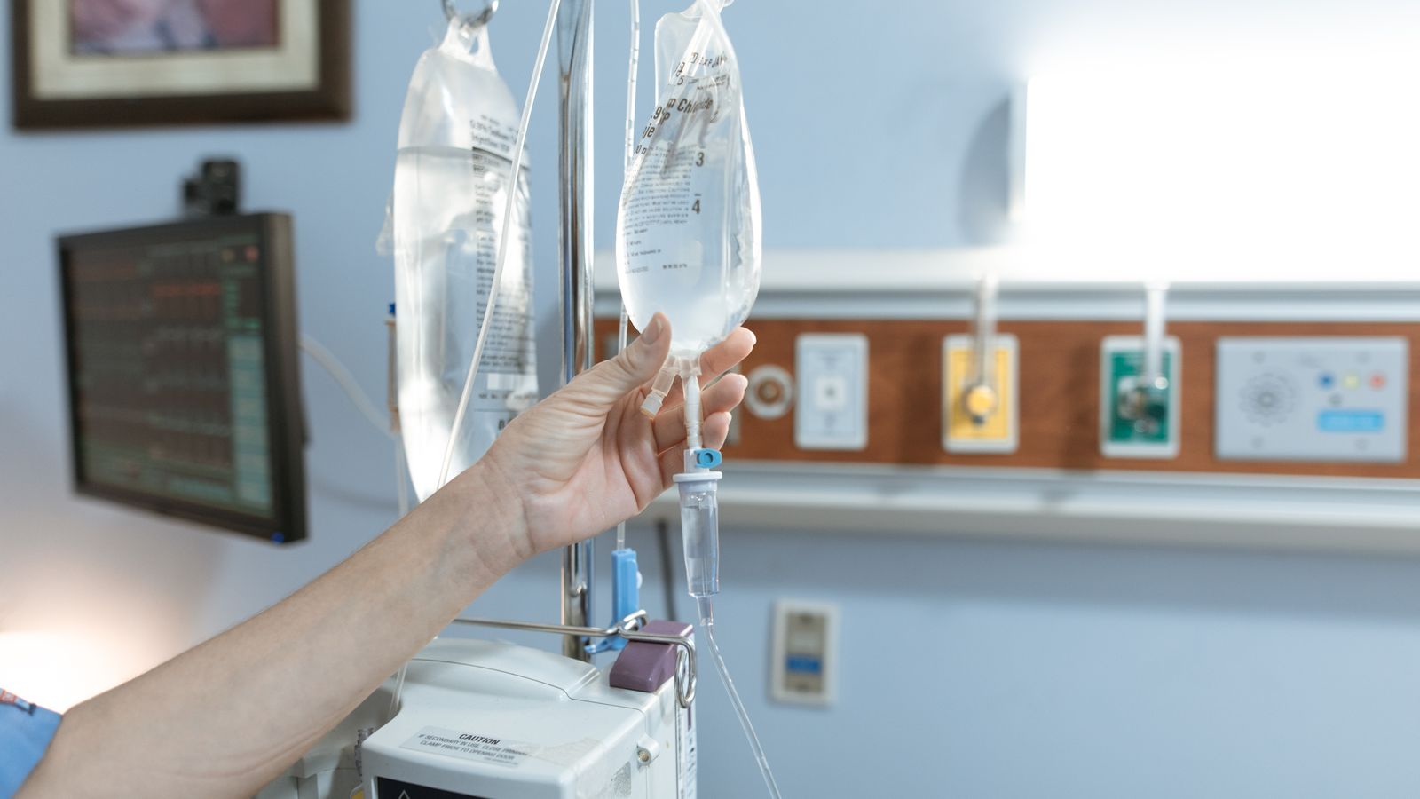 Close-up image of an IV drip and hand in a hospital room, illustrating medical care.