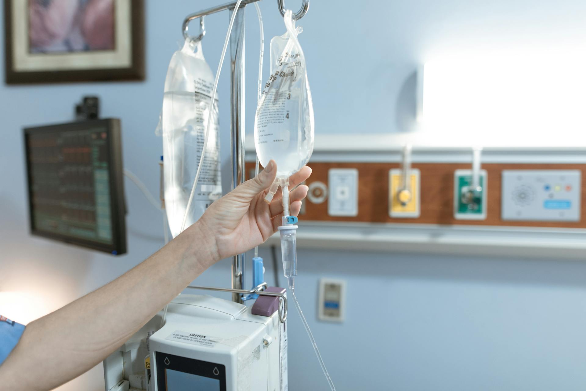 Close-up image of an IV drip and hand in a hospital room, illustrating medical care.